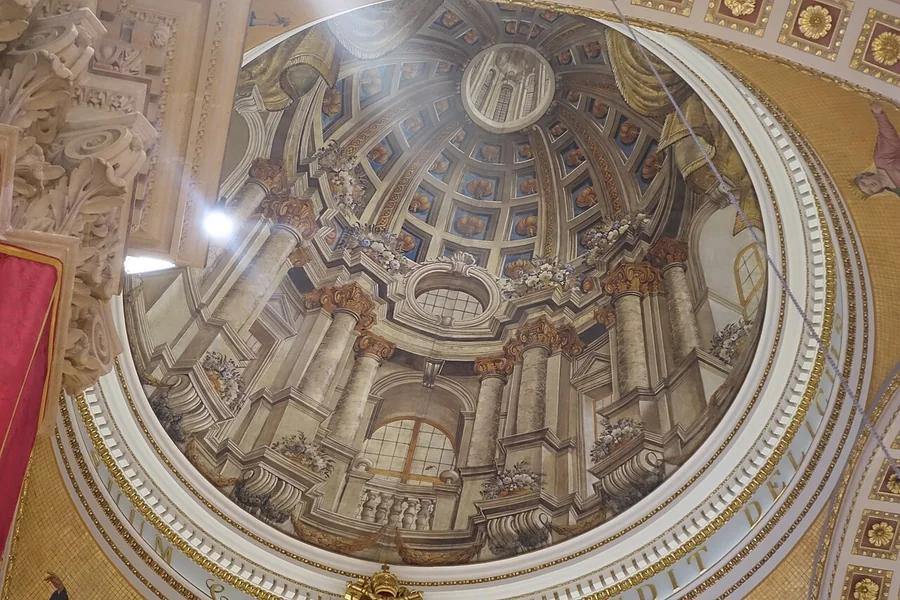 A photograph looking up at the painted ribs and windows of Gozo Cathedral’s false dome.