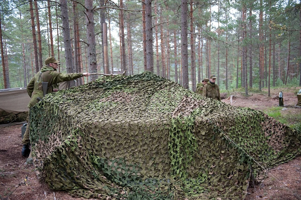 Green and brown camouflage netting draped over a constructed position in a pine woodland.