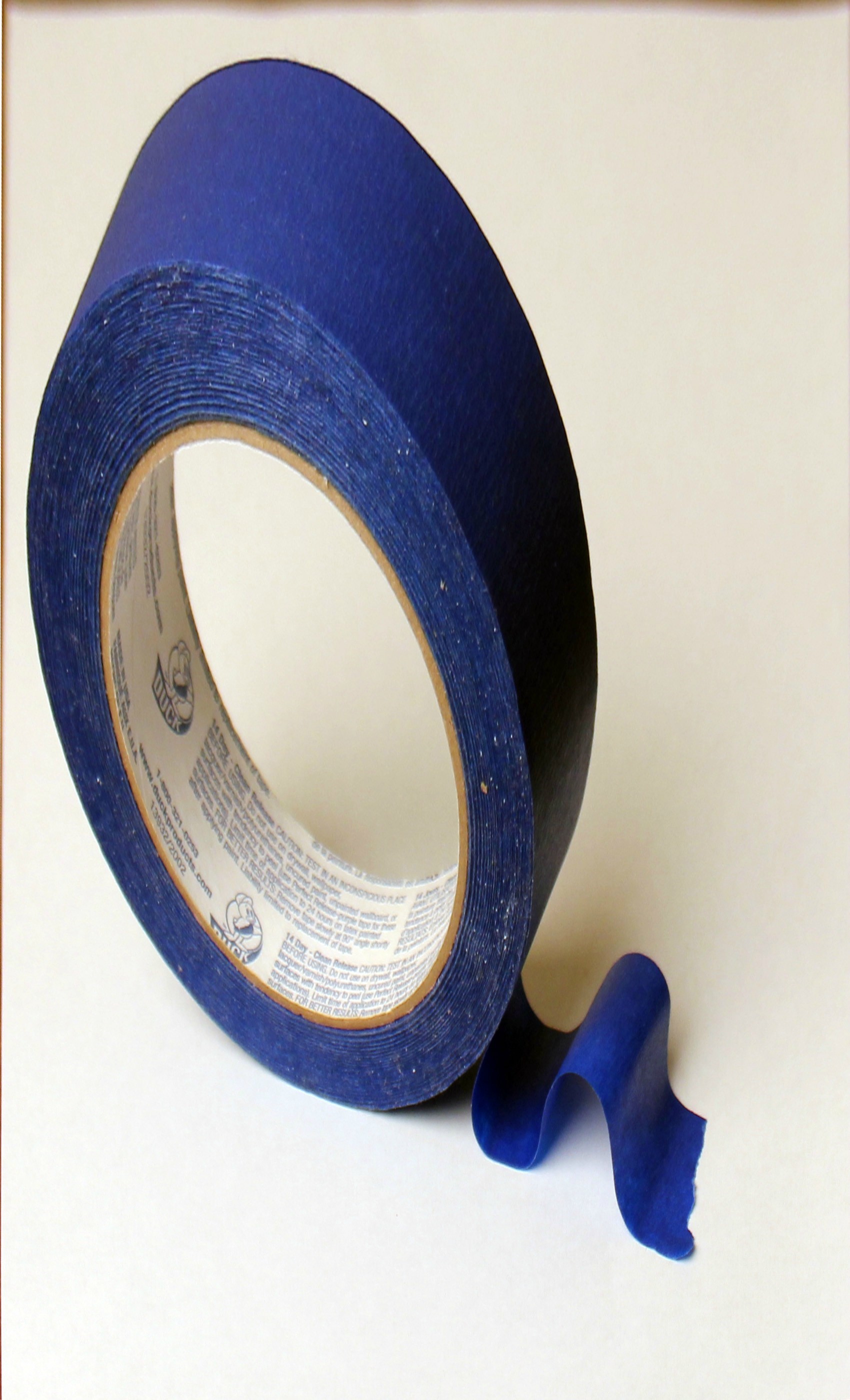 A blue roll of tape casts a shadow on a white surface.