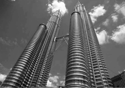 A low-angle black-and-white photograph of tall parallel towers against a cloudy sky.